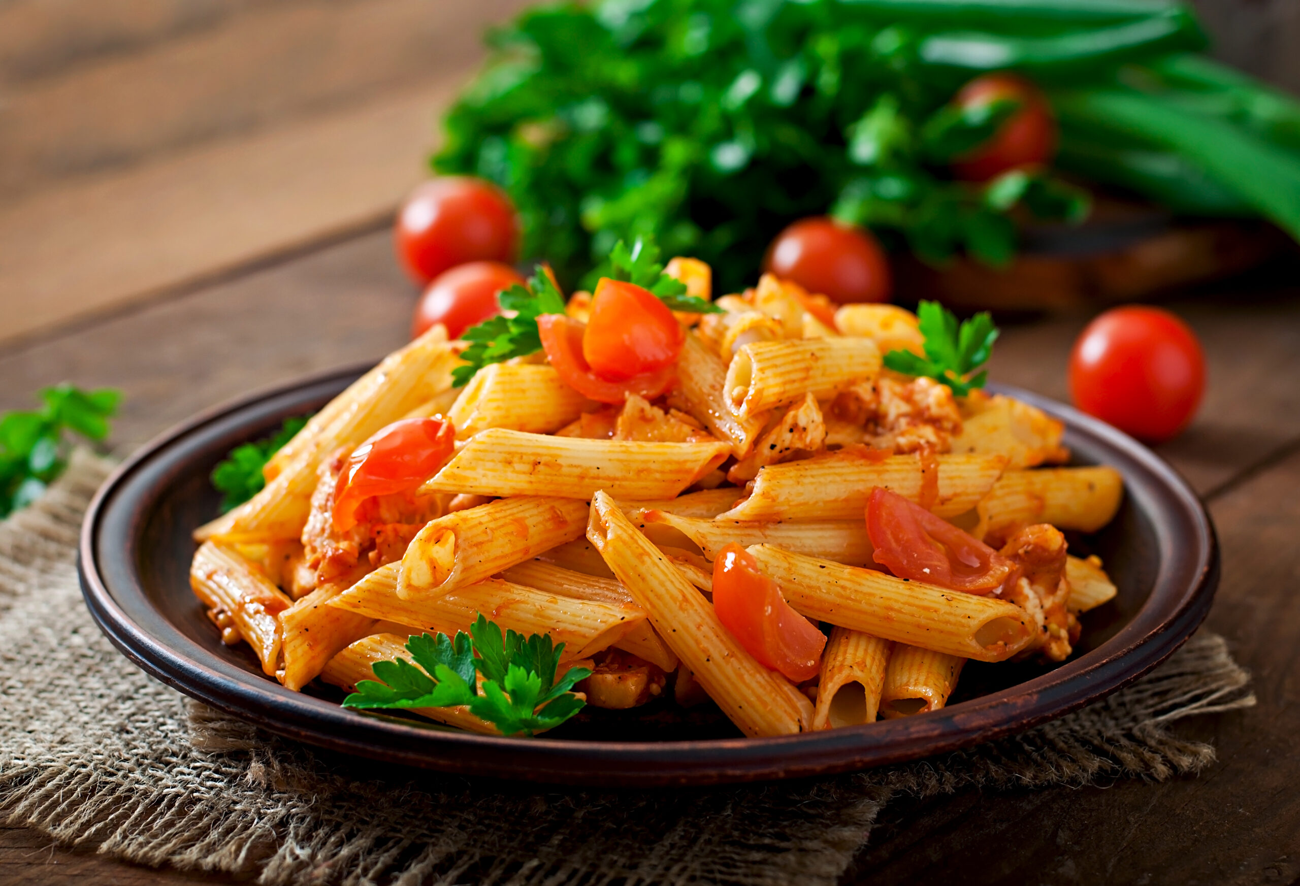 Penne pasta in tomato sauce with chicken and tomatoes on a wooden table